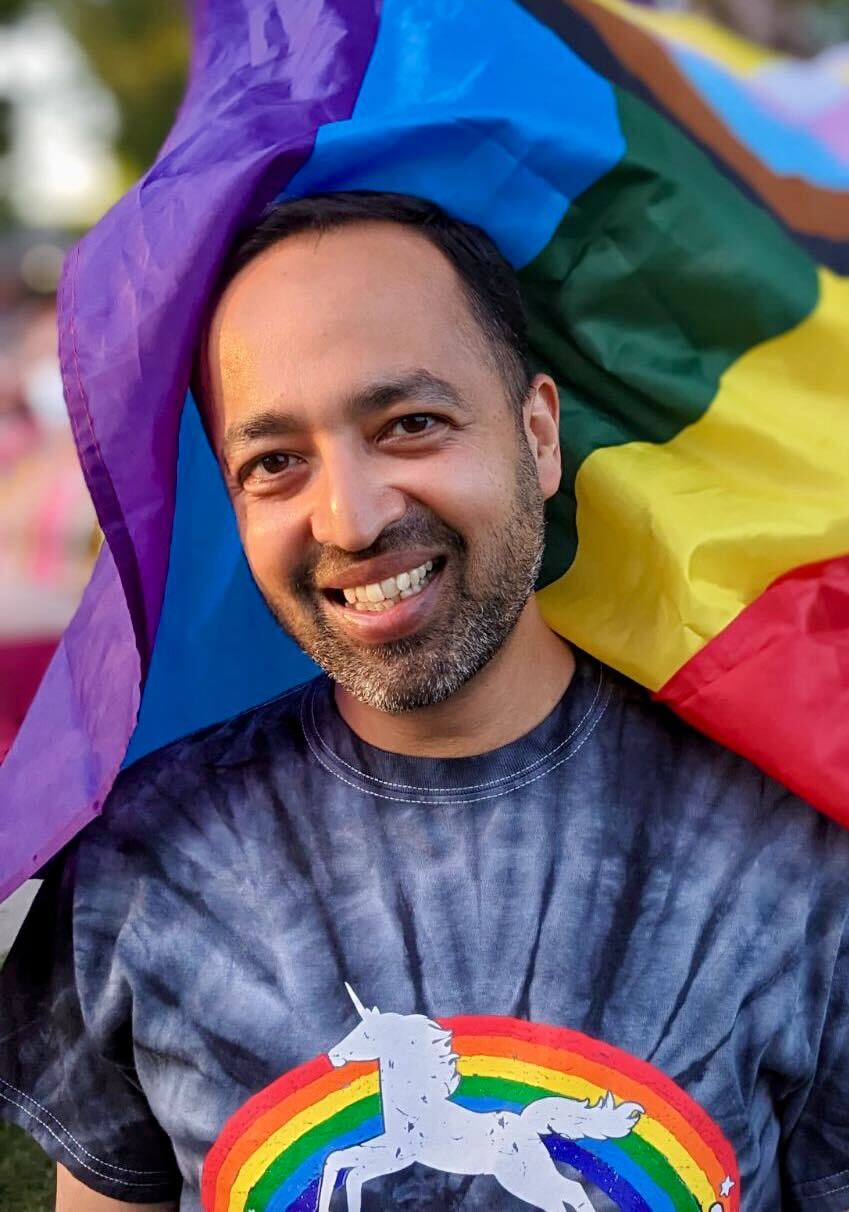 A mugshot of Tanmoy Laskar with a rainbow flag billowing in the background
